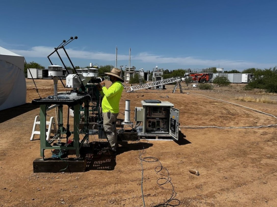 A person wearing a tan hat and bright yellow shirt works outside on radiometers sitting on an instrument platform.