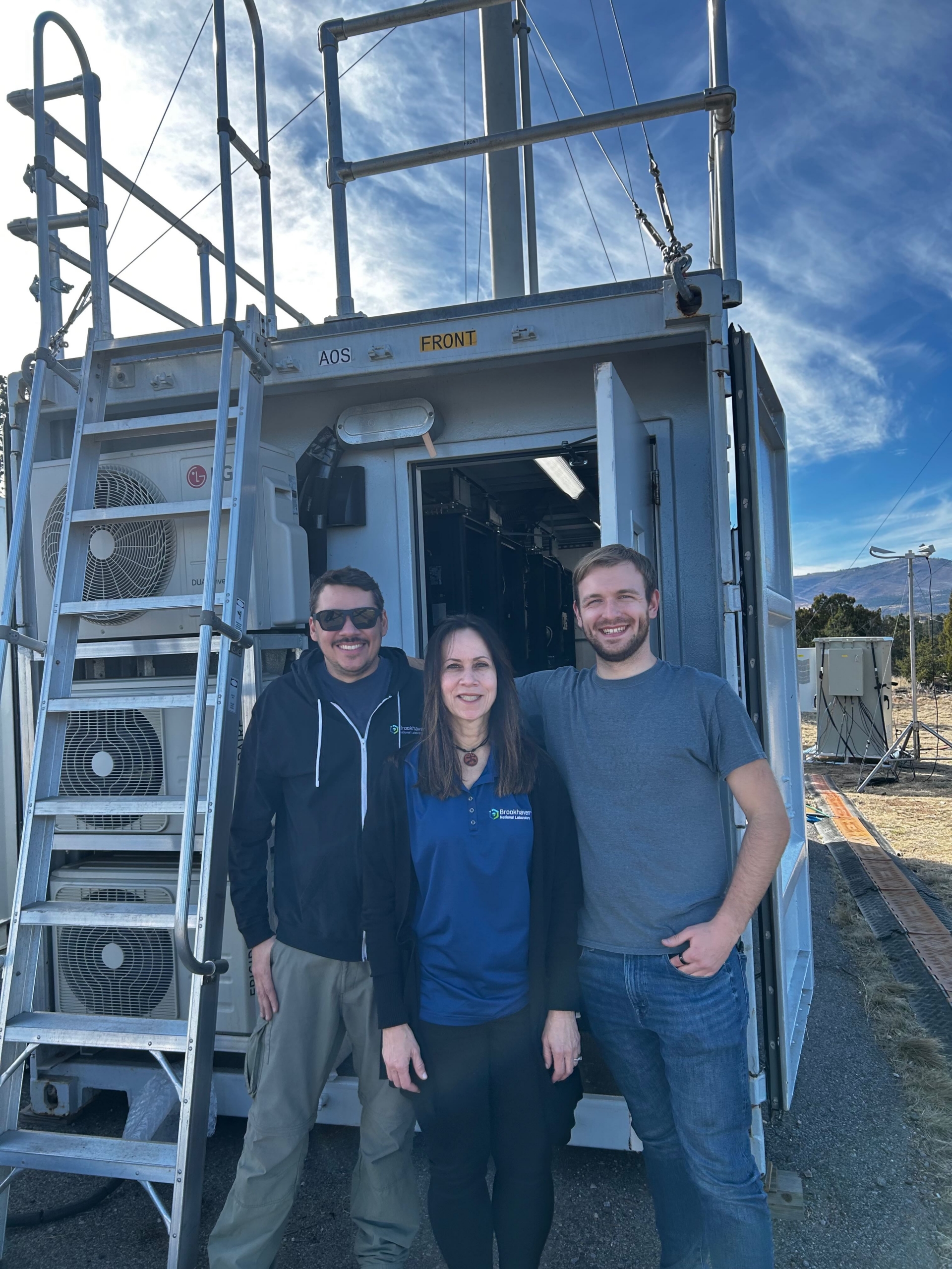 Three people stand in front of the open door of an ARM aerosol instrument container.