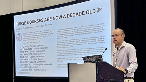 A person stands at a podium with a laptop open and a large screen to their side that shows a schedule for the past 10 years of ERAD/AMS open source radar software short courses.