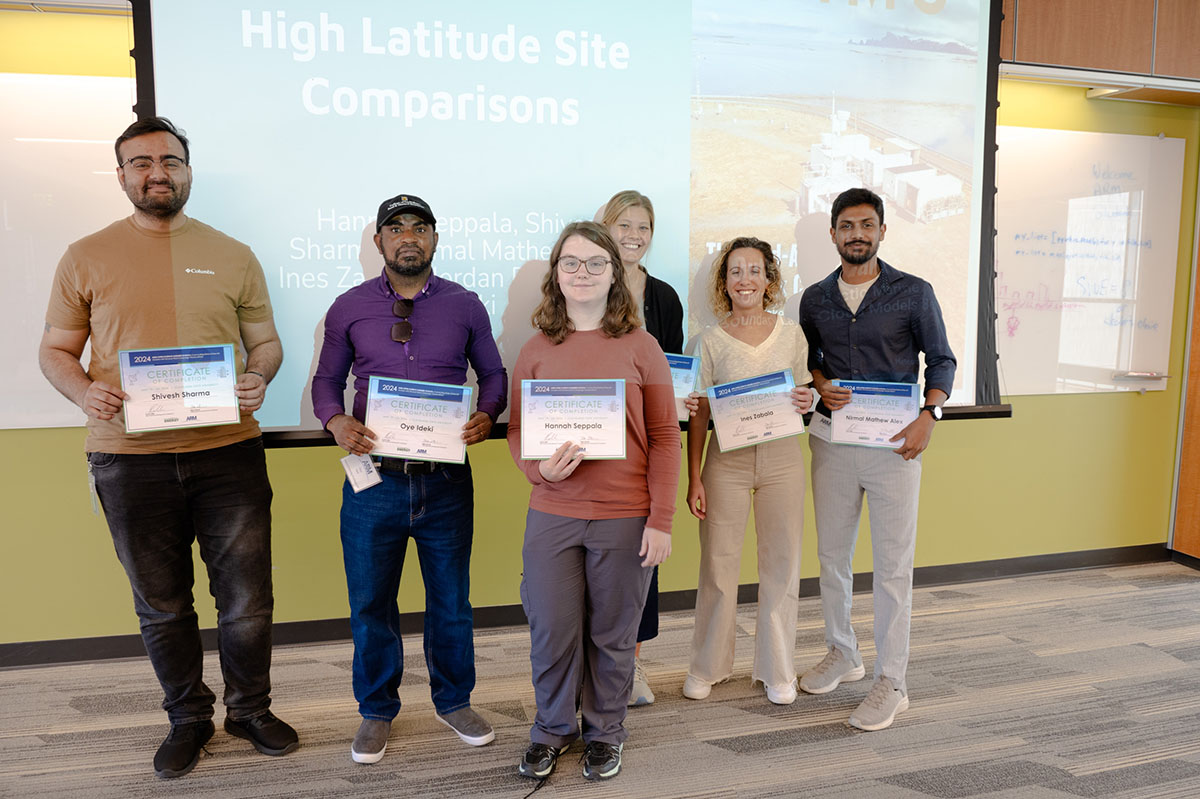 Six people hold certificates while standing in front of a slide that says,