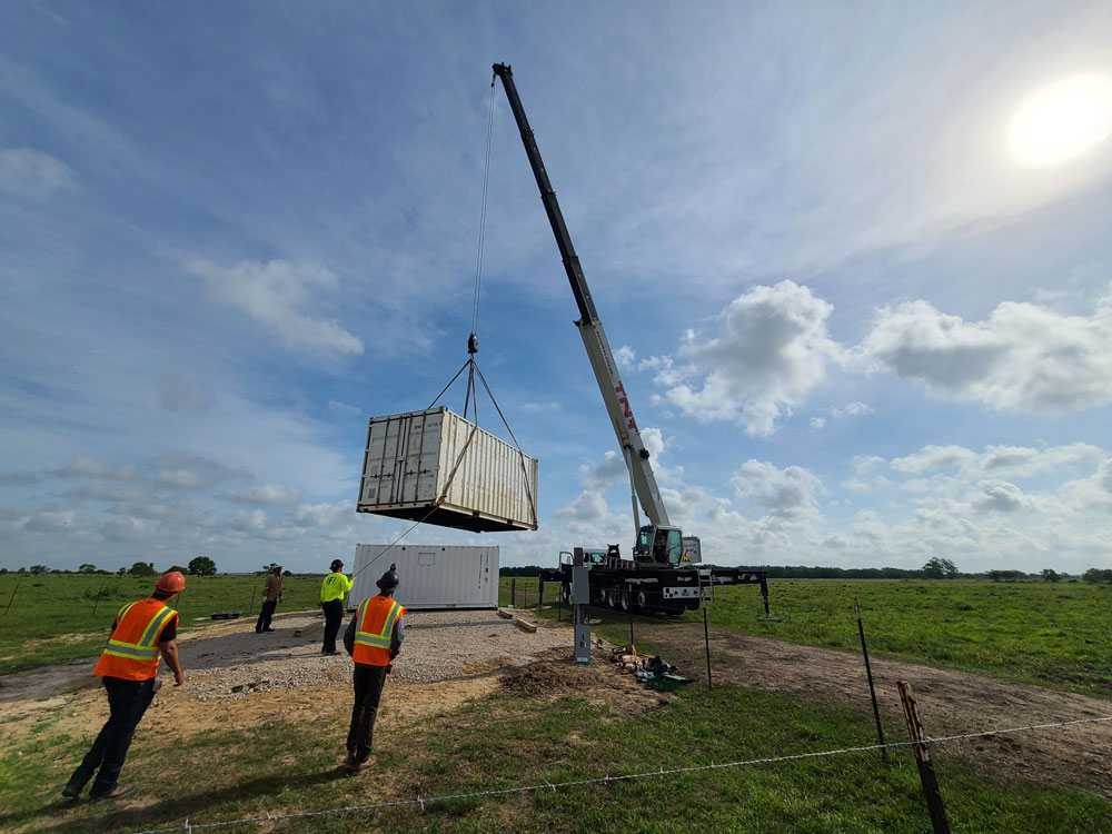 One technician helps lower a container strapped to a crane while three others stand watch.