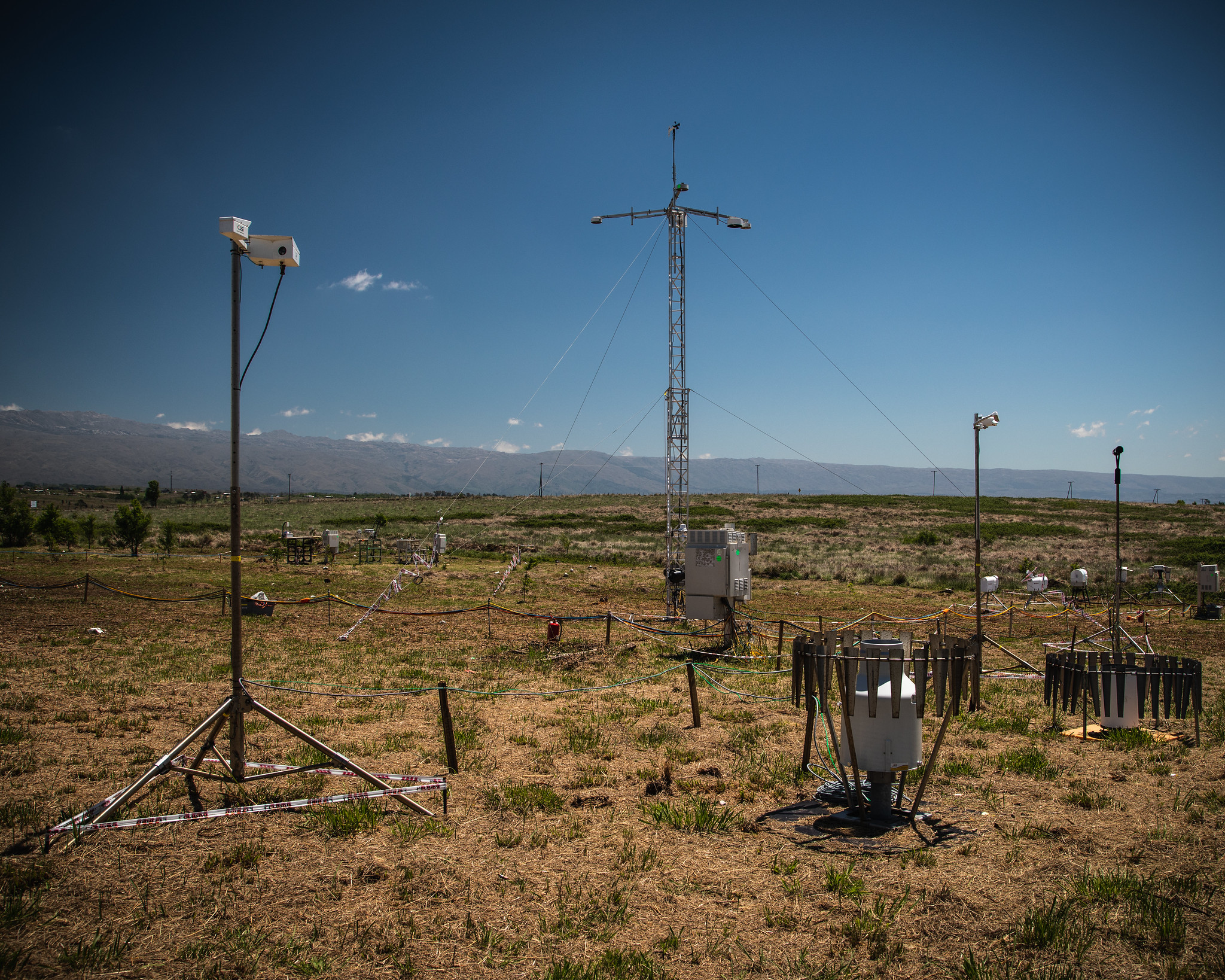 Precipitation instruments stand in a field with mountains in the distance.