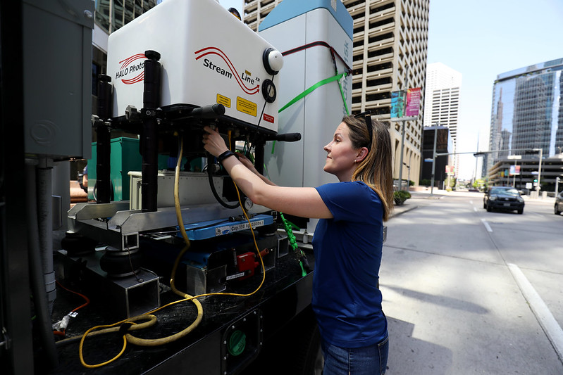 An atmospheric scientist adjusts an instrument that is installed on a mobile laboratory on a downtown street.
