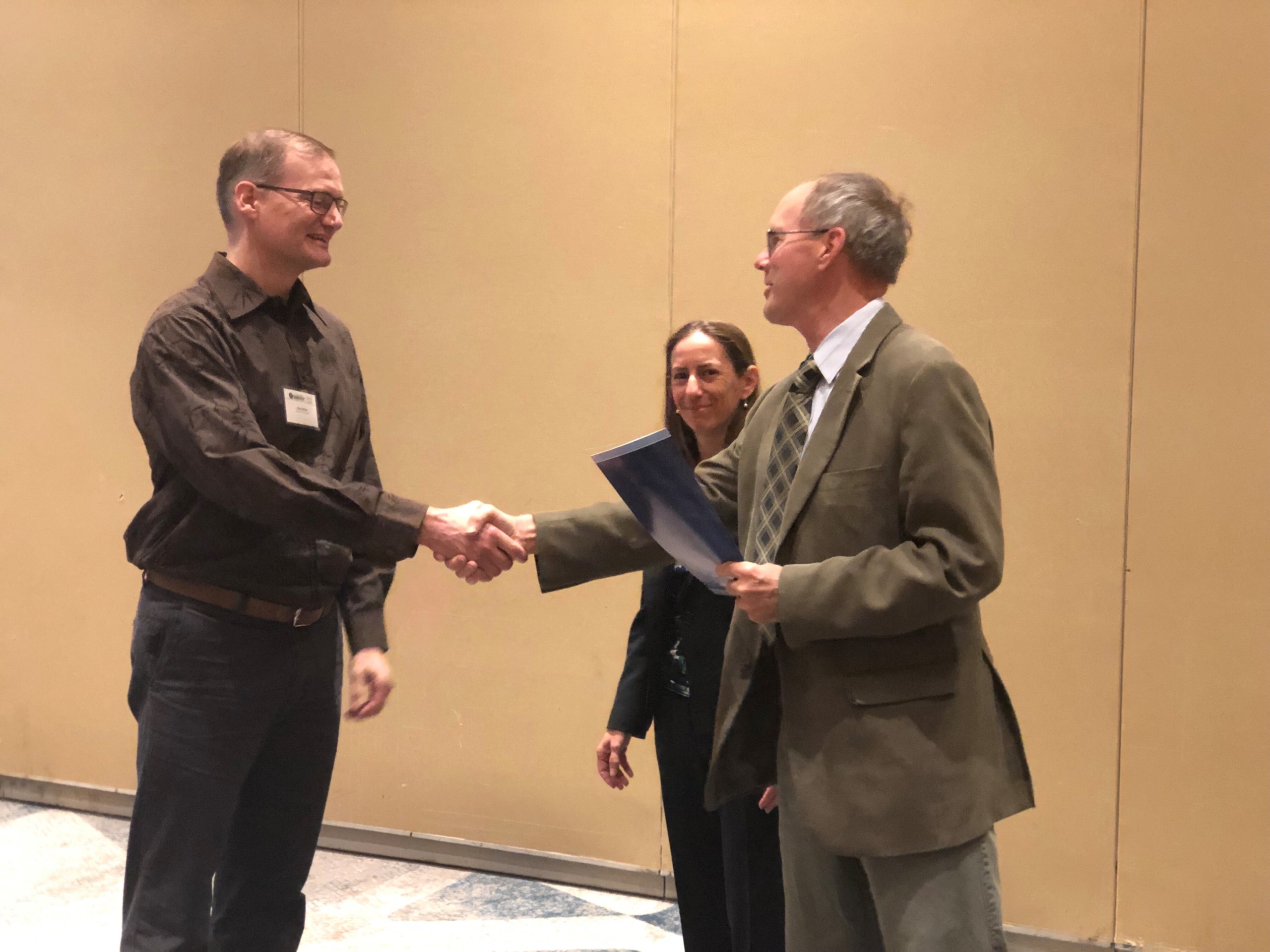 Two people shake hands with a third person looking on in the middle.