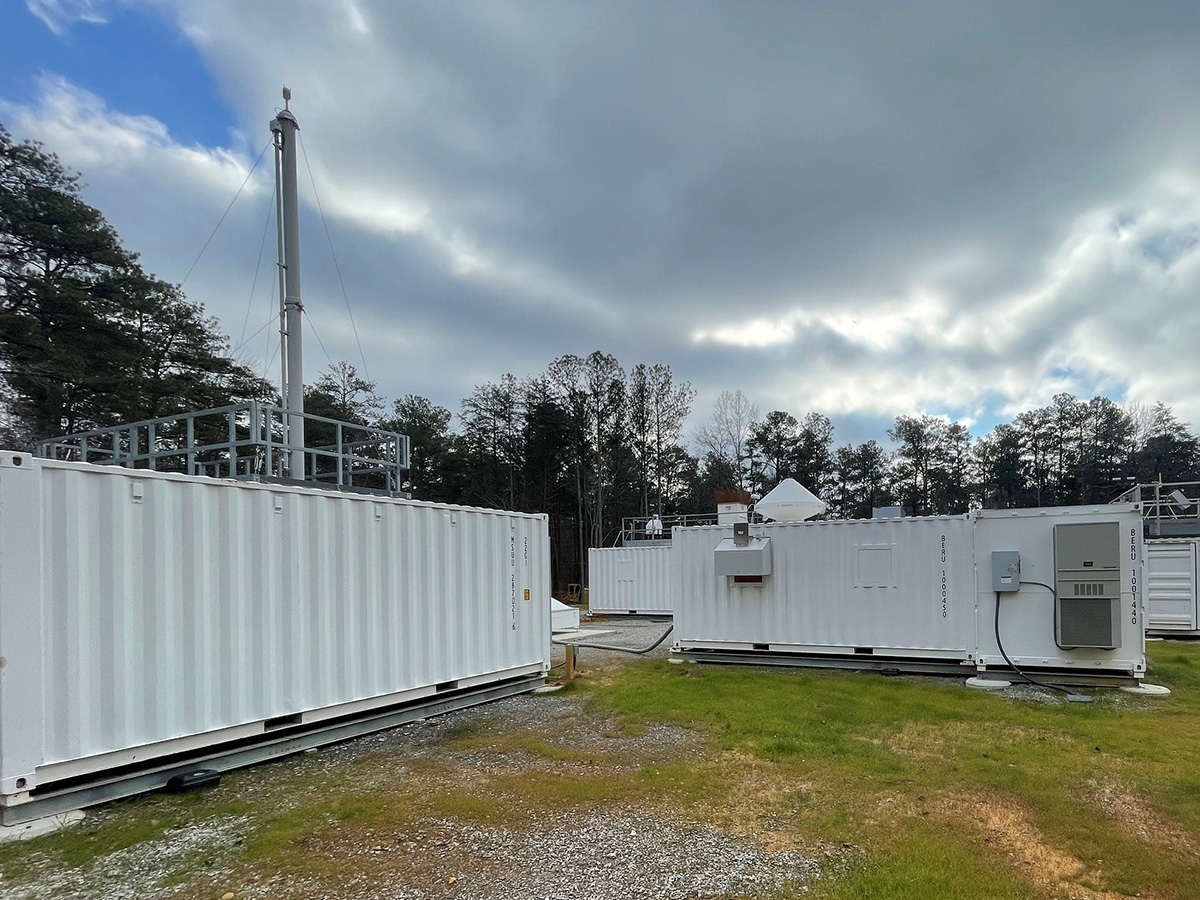 The Bankhead National Forest Aerosol Observing System (left) and Ka-Band ARM Zenith Radar (on the roof of the instrument container to the right) are shown on a cloudy day. The forest is visible above and between the instrument containers.