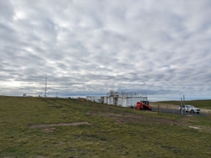 Containers holding atmospheric instruments sit on a green grassy field with a cloudy sky above