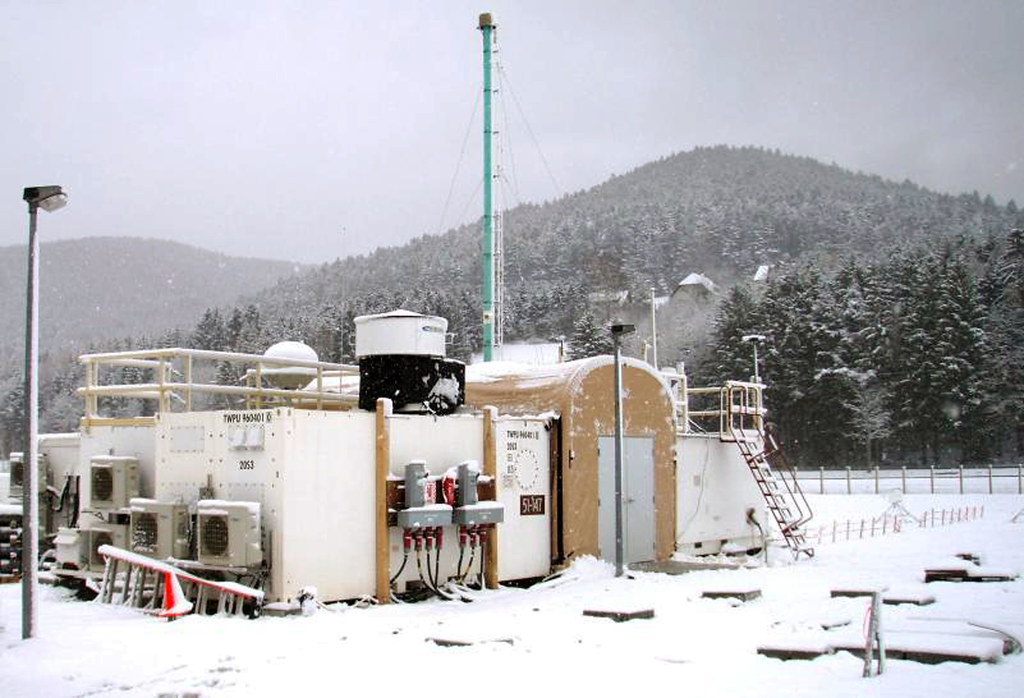 Snow falls on the ARM Mobile Facility’s primary operations shelter and forested hills behind it.