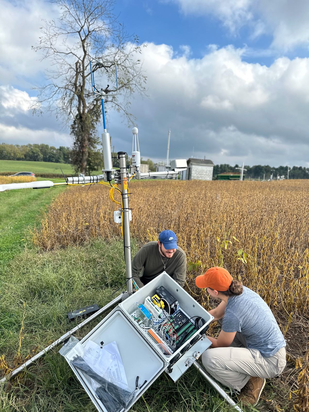 Two kneeling people work on an instrument in a grassy field.