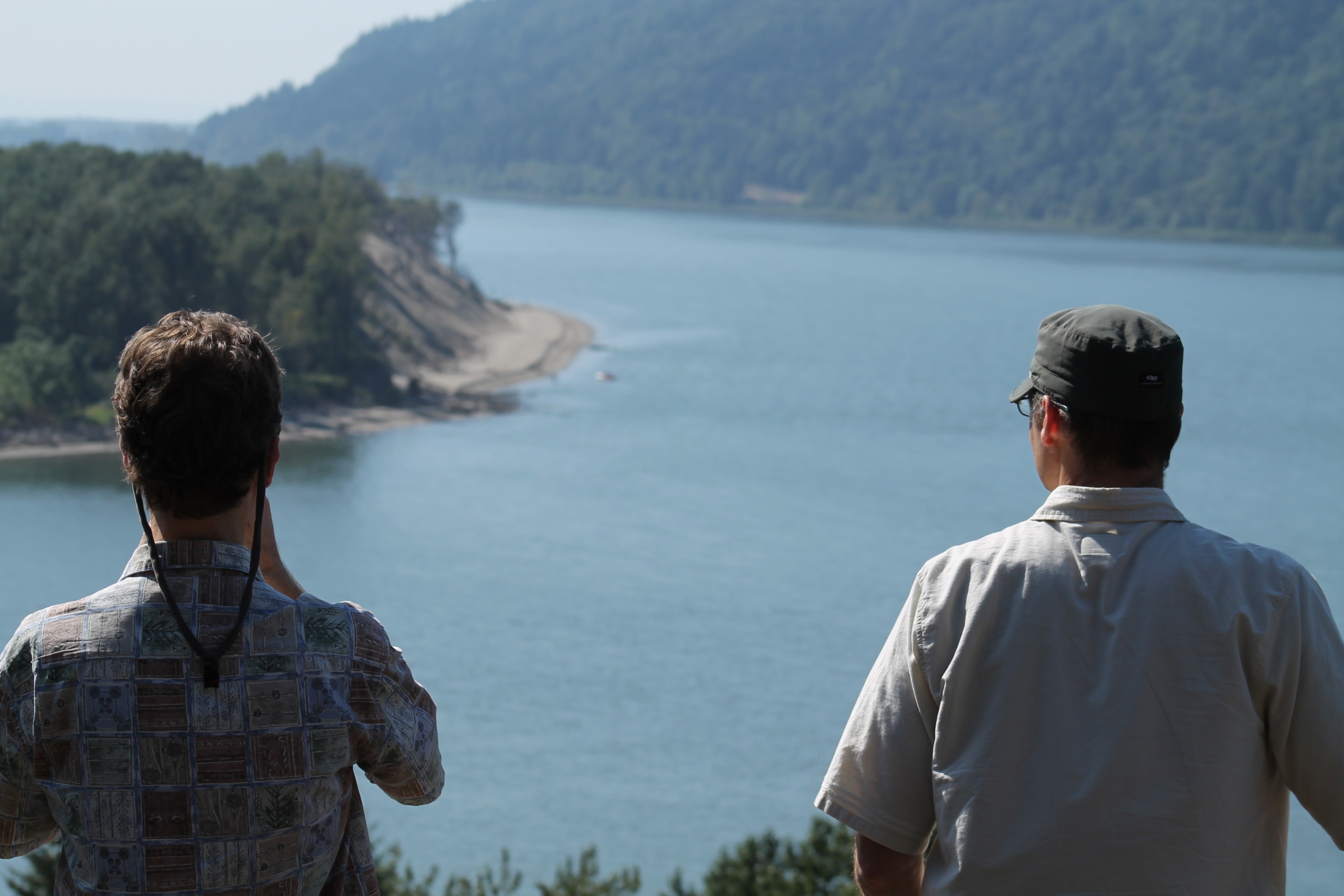 Two people look out over a tree-lined river.