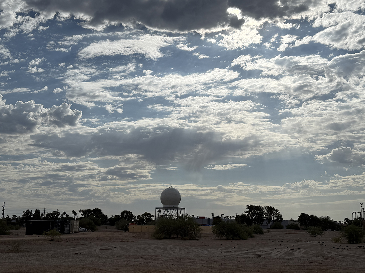 A radar protrudes above several bushes along the ground. Clouds streak across the sky.