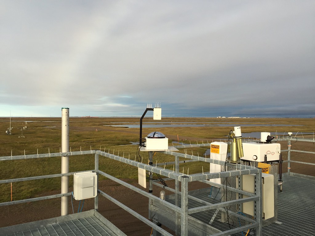 A total sky imager, Doppler lidar, and Cimel sunphotometer are on a rooftop overlooking snow-free Alaskan tundra.