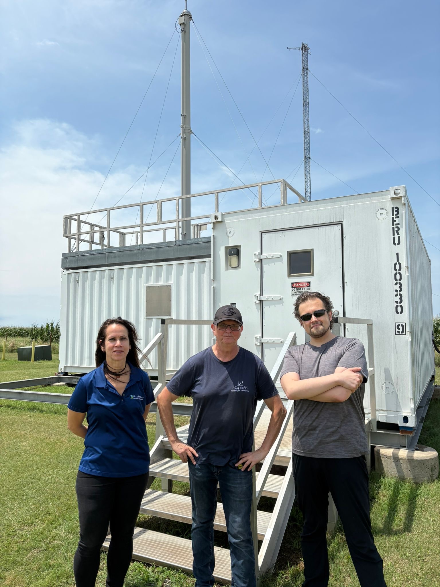 Three people stand in front of an ARM Aerosol Observing System.