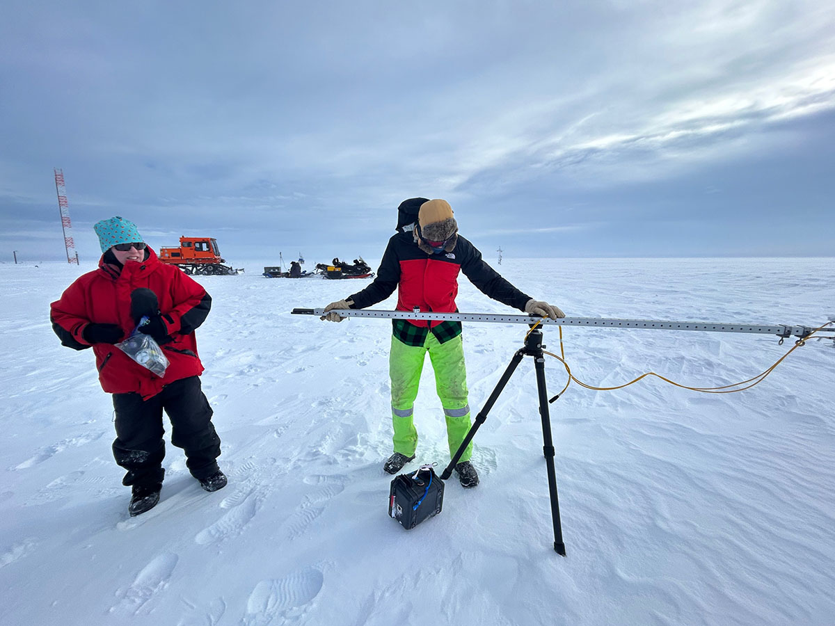 Two people work with equipment on snow.