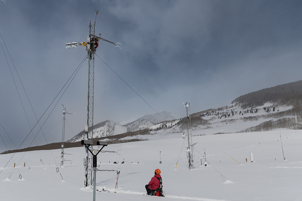 A person crouching down looks up at a colleague working on a tower.