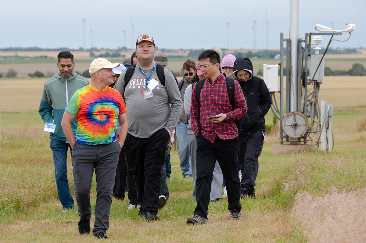 A group of people walks near atmospheric instruments in a large grassy field on an overcast day.