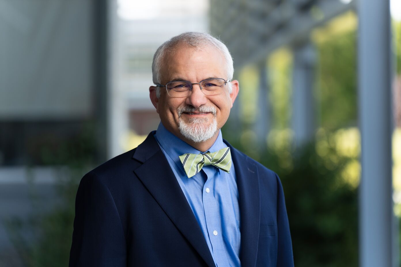 Portrait of Larry Berg wearing a green bowtie with stripes, a blue dress shirt, navy blazer, and glasses