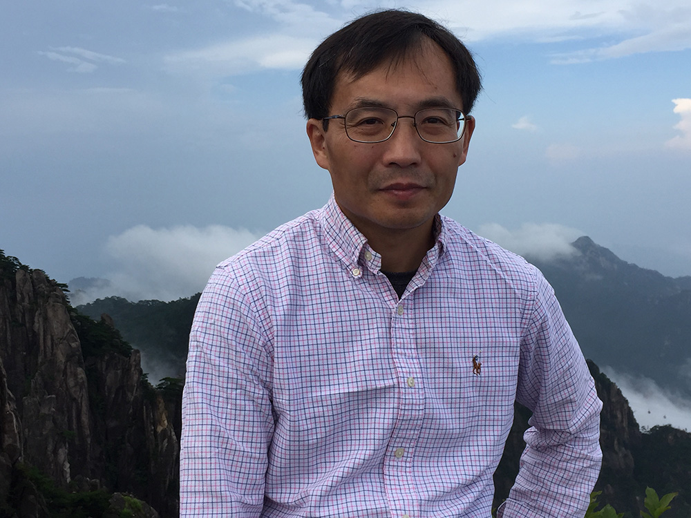 Zhien Wang poses in front of mountains during a hike on a cloudy day.