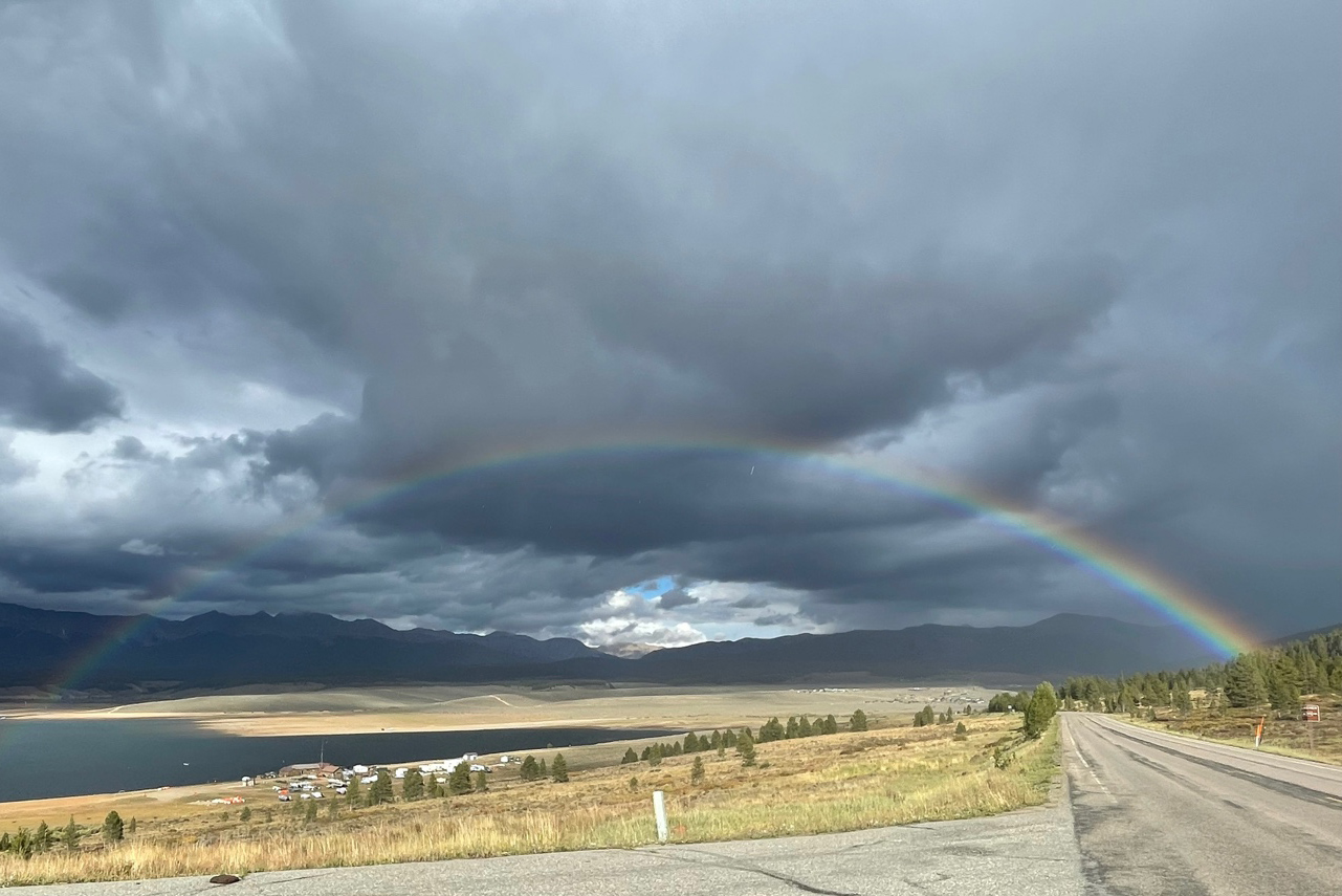 Amid dark clouds, the sun peeks through the middle of a rainbow.